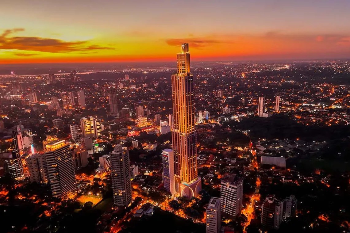 Luftaufnahme der Skyline von Asunción in der Abenddämmerung mit einem beleuchteten Hochhausturm im Zentrum